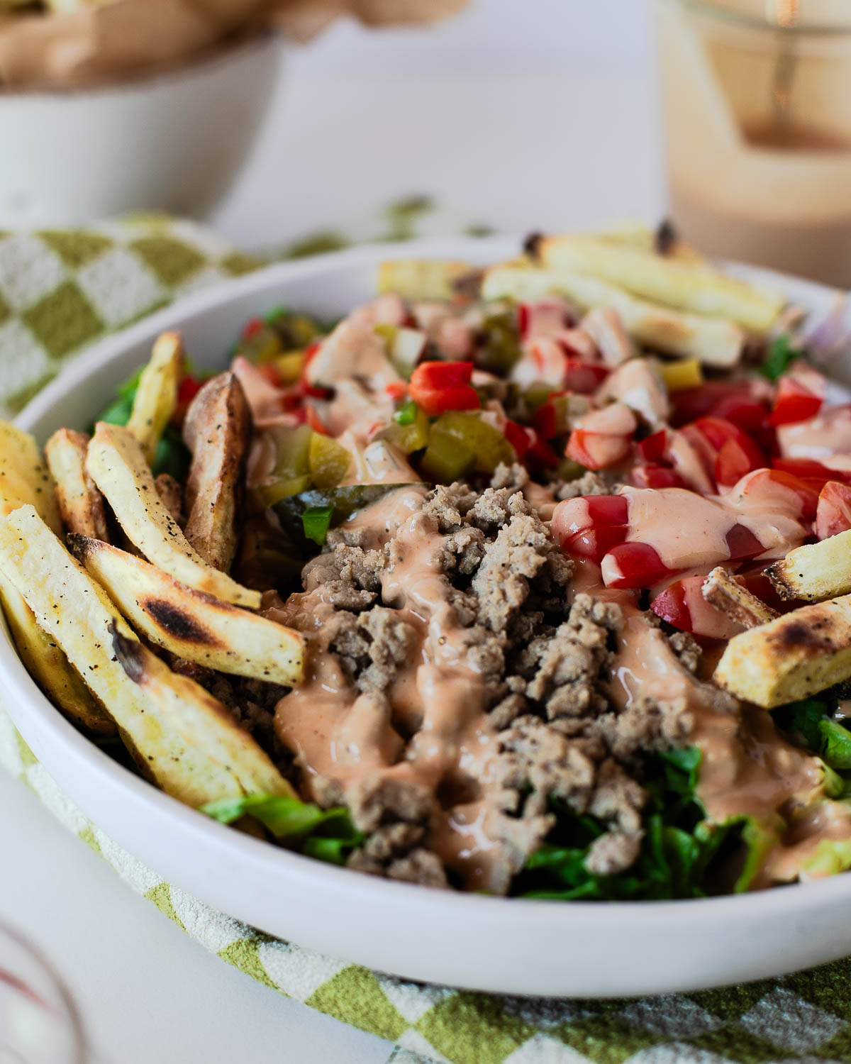Side view of a healthy burger bowl featuring seasoned turkey, fresh romaine lettuce, tomatoes, sweet potato fries, and tangy burger sauce.