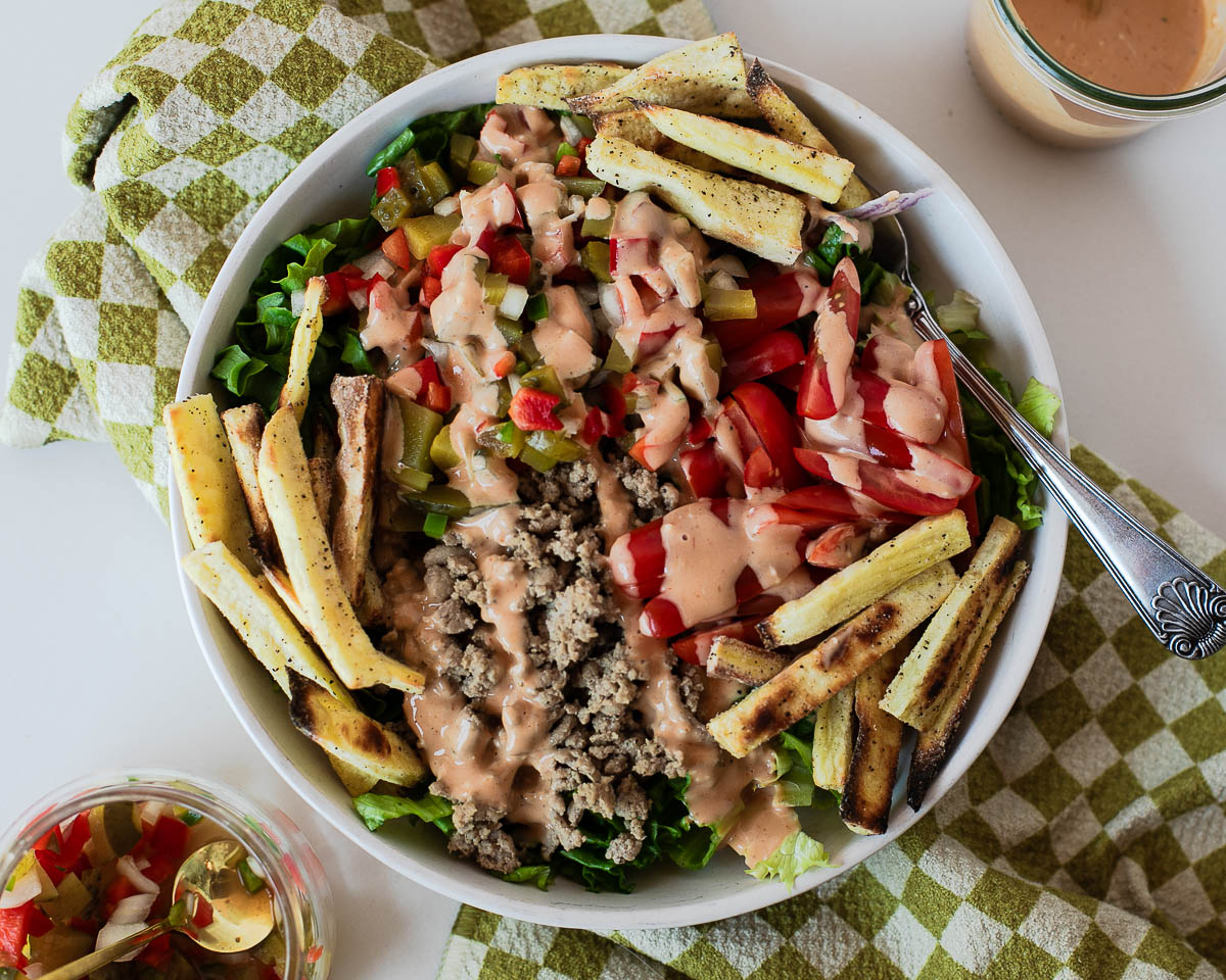 Overhead view of a turkey burger bowl with romaine lettuce, tomatoes, pickle de gallo, sweet potato fries, and homemade special sauce.
