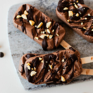 Chocolate protein popsicles topped with melted chocolate and chopped peanuts, featuring a rich, creamy texture and high-protein ingredients.