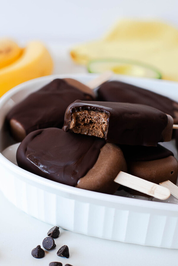 Creamy chocolate avocado popsicles with dark chocolate coating and a bite taken out.