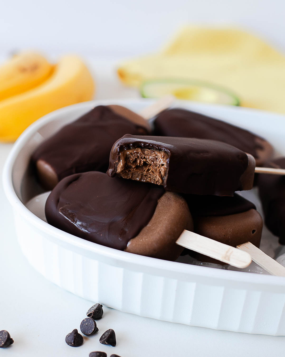 Creamy chocolate avocado popsicles with dark chocolate coating and a bite taken out.