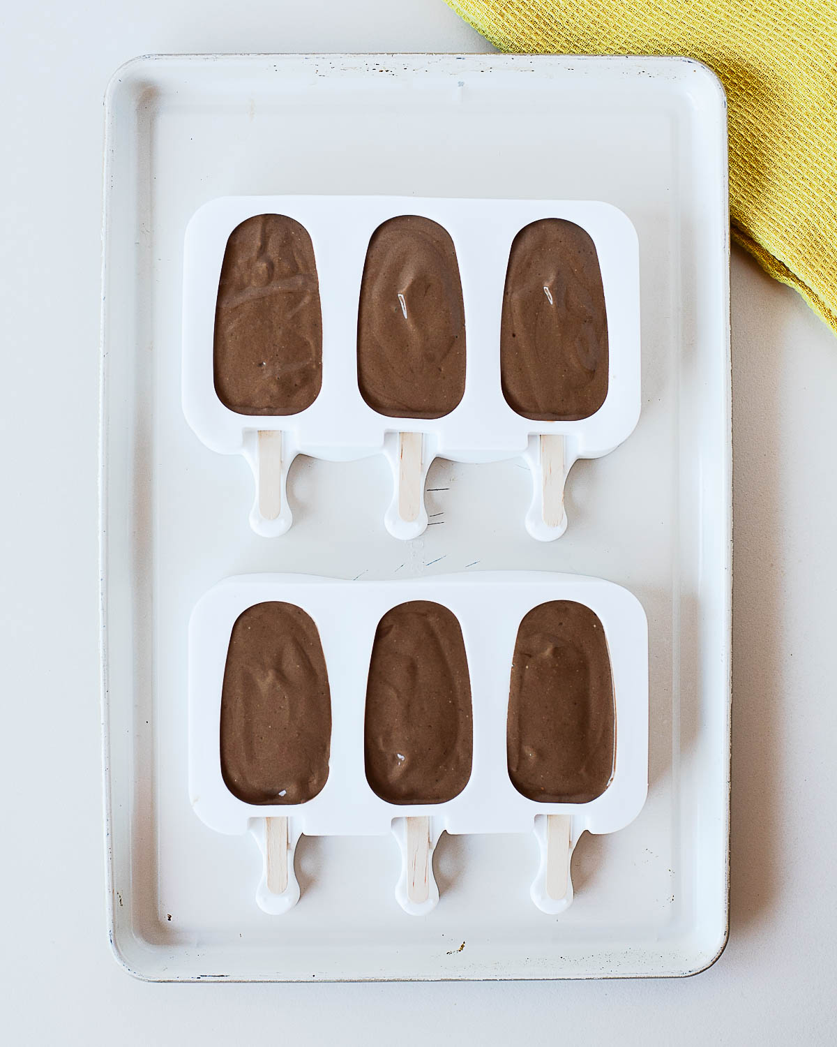 Chocolate avocado popsicle mixture poured into six white popsicle molds.