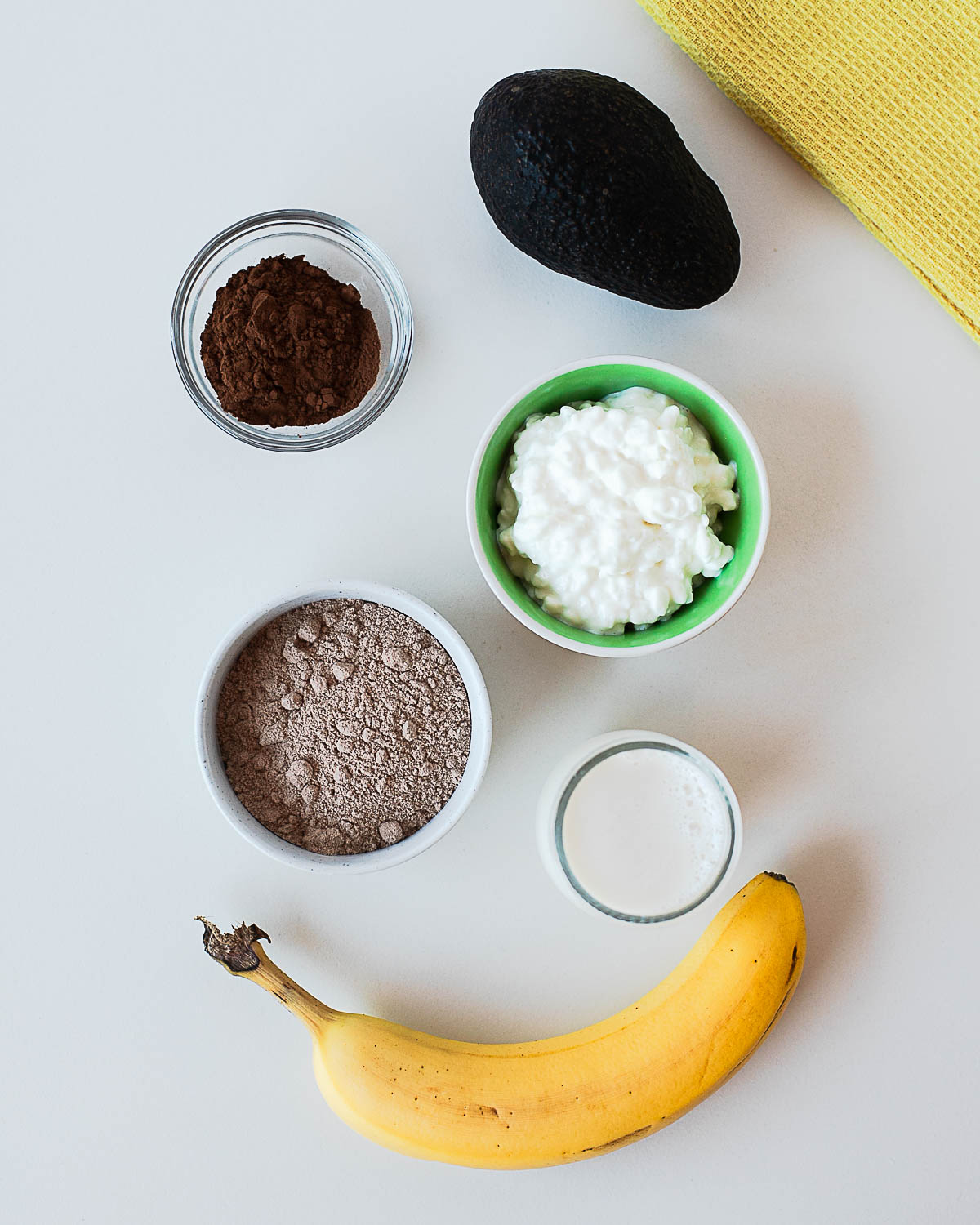 Ingredients for chocolate avocado popsicles including avocado, banana, cottage cheese, almond milk, chocolate protein powder, and cocoa powder.