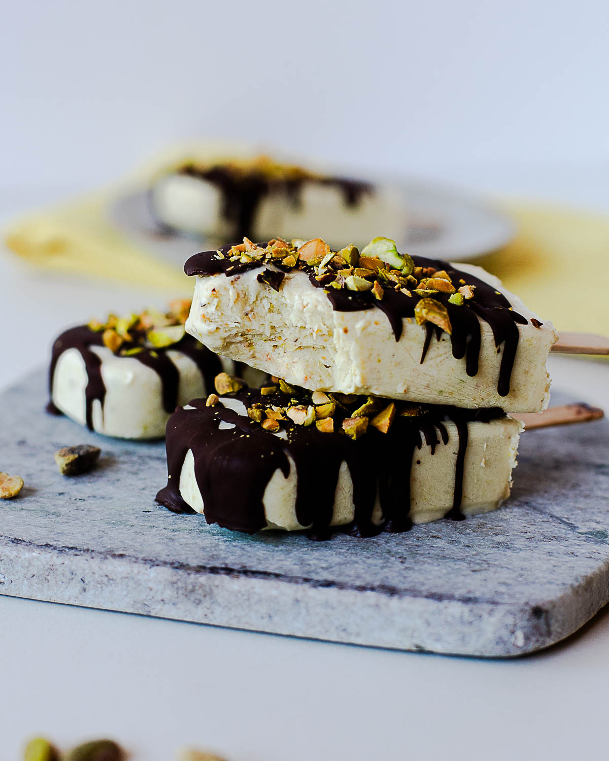 Stack of creamy pistachio popsicles with melted dark chocolate and chopped pistachios.
