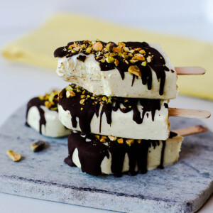 Stacked pistachio protein popsicles with a dark chocolate drizzle and crunchy pistachio topping.