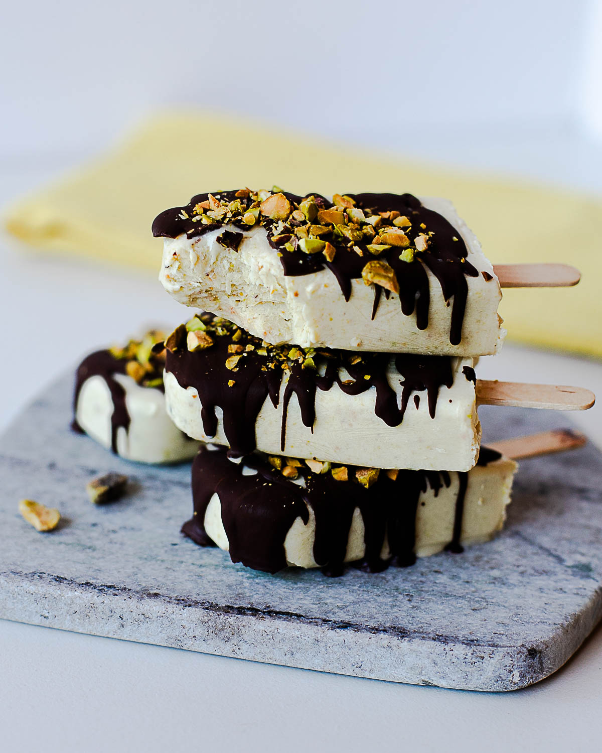 Stacked pistachio protein popsicles with a dark chocolate drizzle and crunchy pistachio topping.