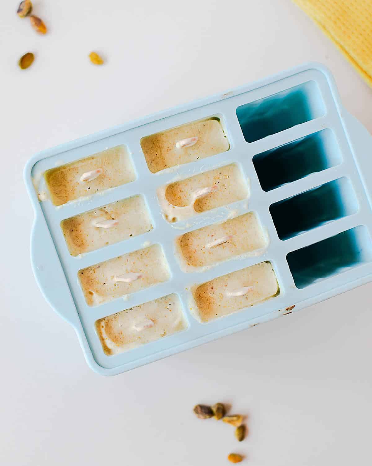 Frozen homemade pistachio popsicles in a silicone mold with wooden popsicle sticks.