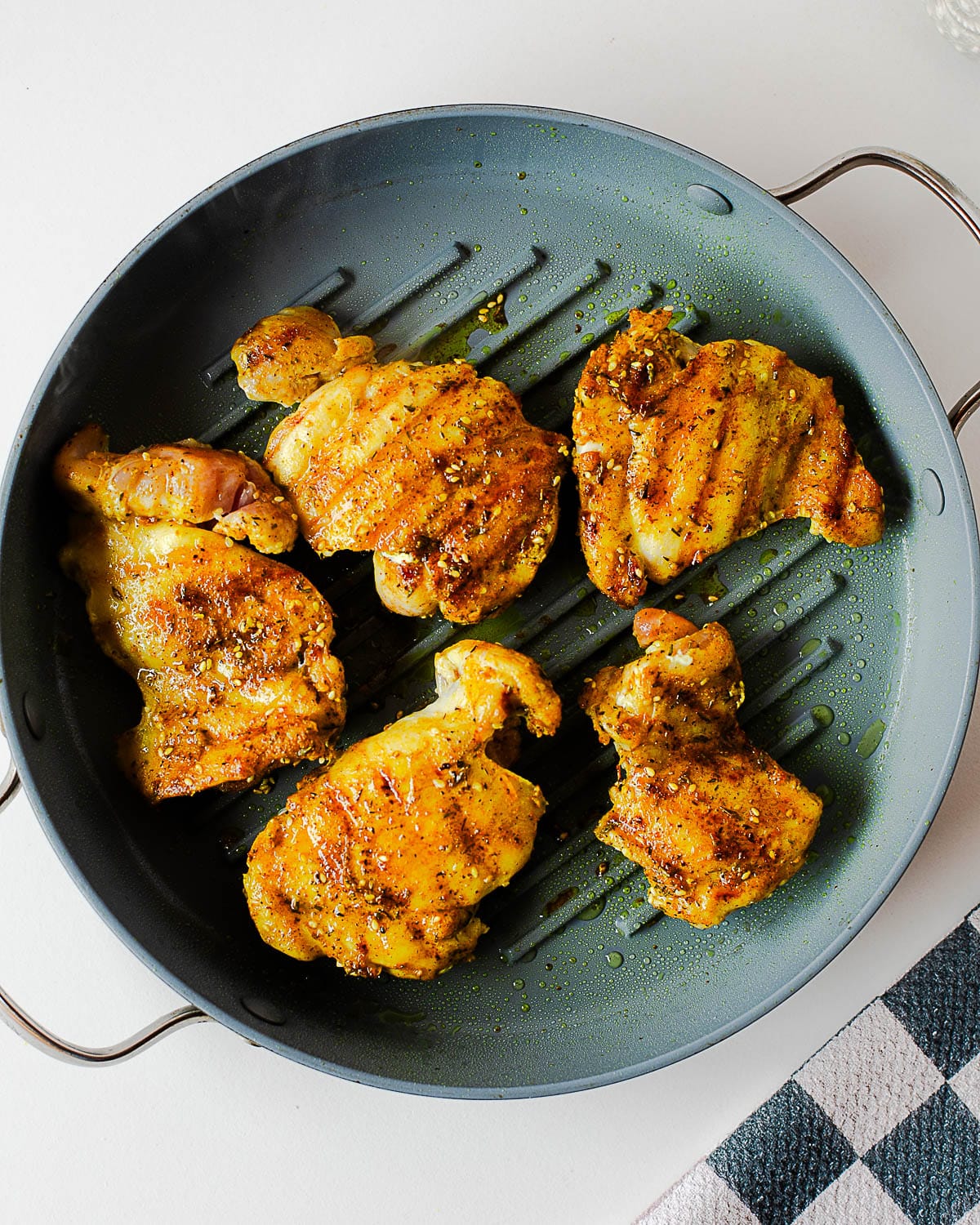 Za’atar chicken thighs searing in a hot grill pan until golden brown with visible grill marks.