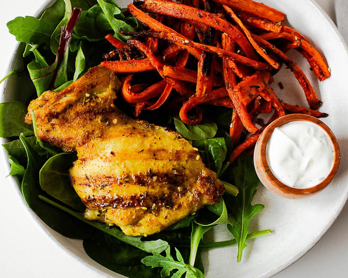 Close-up of za’atar chicken thigh with roasted carrots, mixed greens, and creamy sauce for an easy dinner.