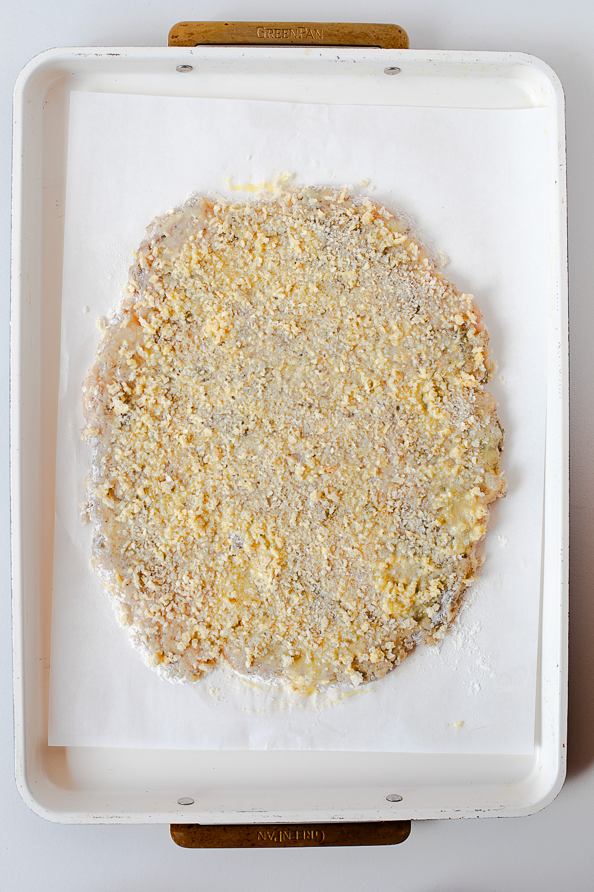 Raw panko-parmesan crusted chicken cutlet on a parchment-lined baking sheet before baking