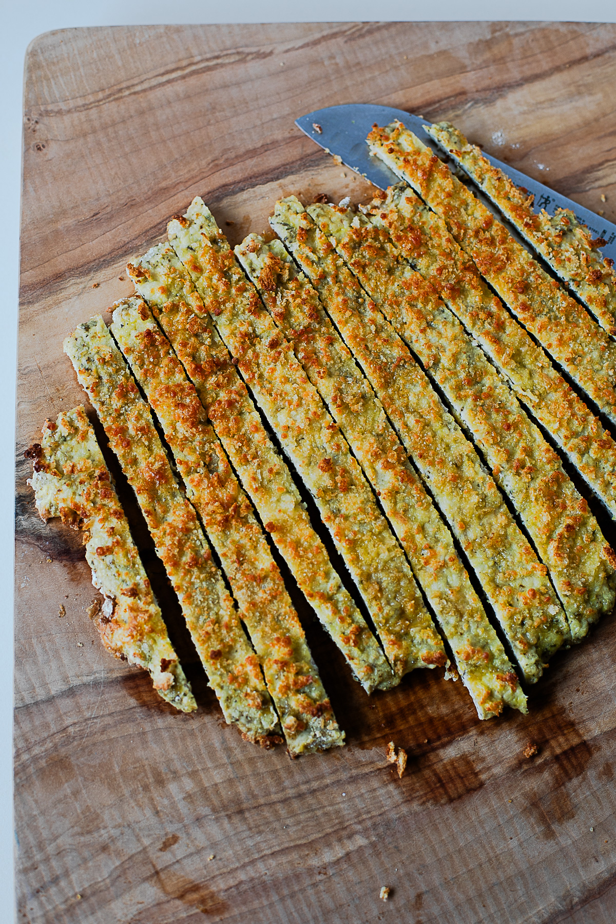 Crispy baked chicken cutlet sliced into strips on a wood cutting board