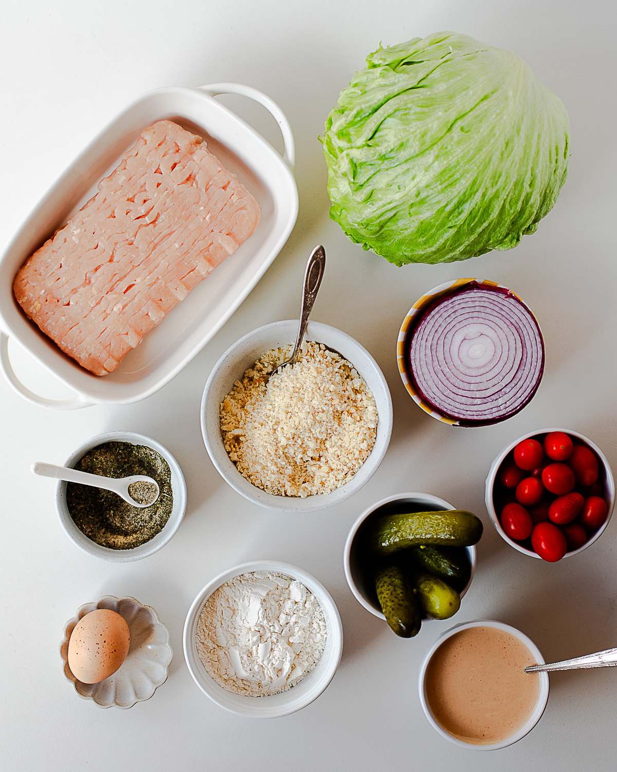 Ingredients for chicken cutlet bowl including ground chicken, panko, seasoning, flour, egg, lettuce, tomatoes, onion, pickles, and burger sauce
