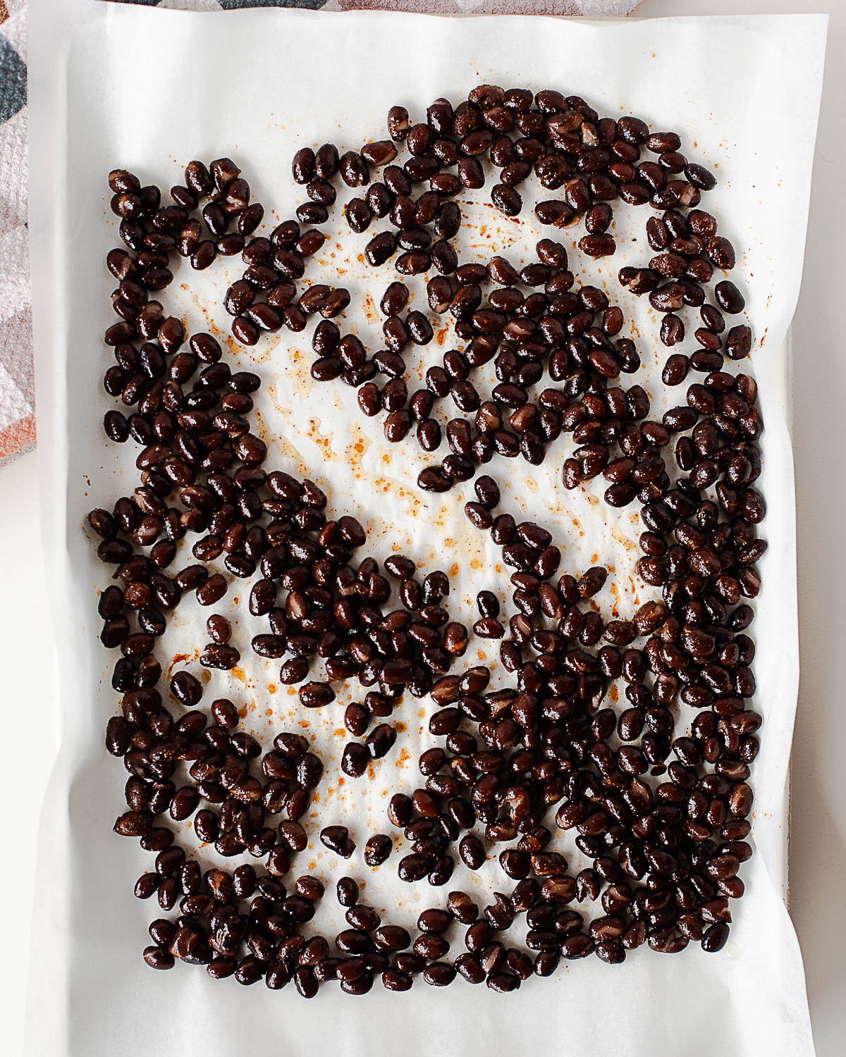 Seasoned black beans spread in a single layer on a parchment-lined baking sheet before roasting.