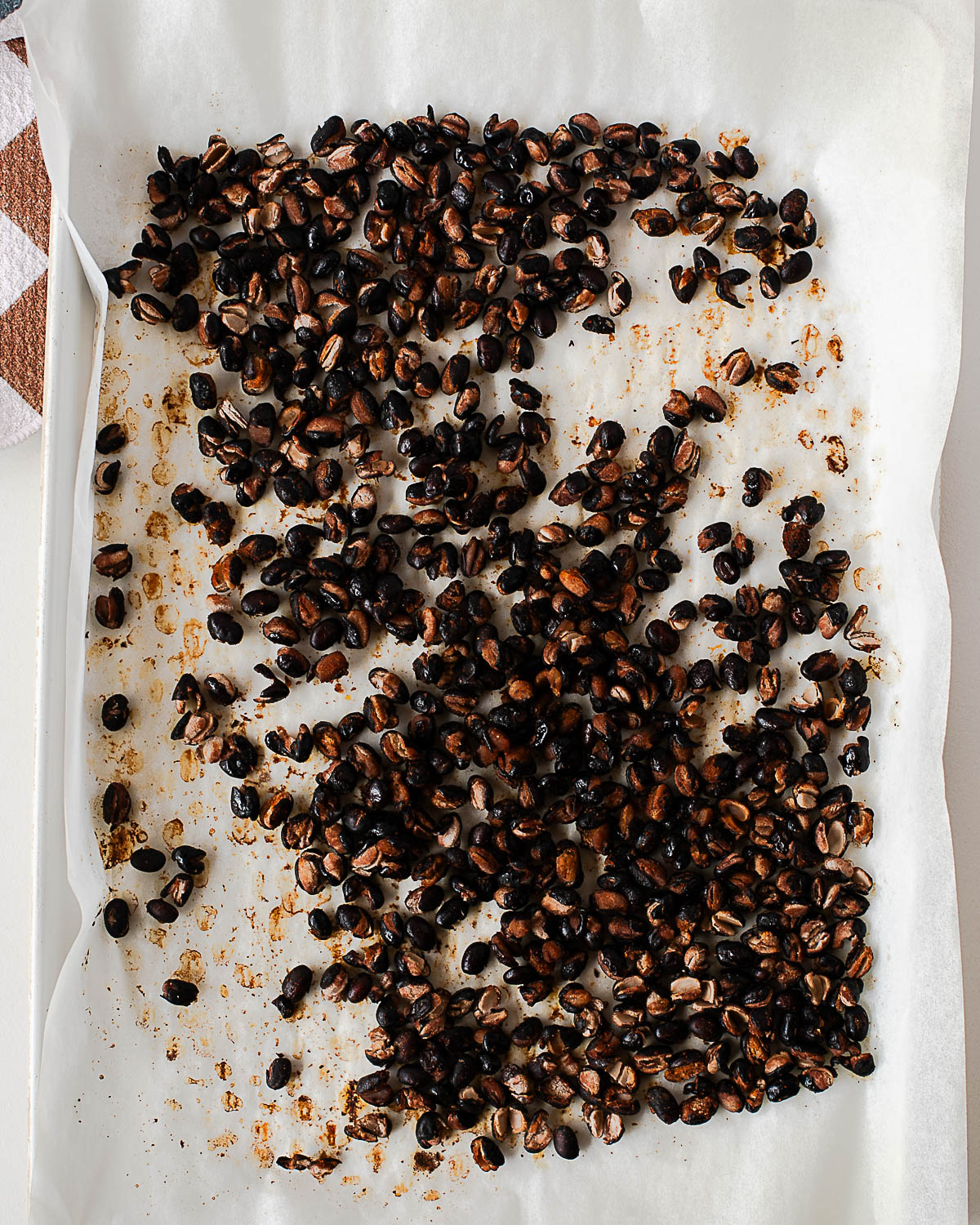 Crispy roasted black beans with split, golden-brown edges on a parchment-lined baking sheet fresh from the oven.