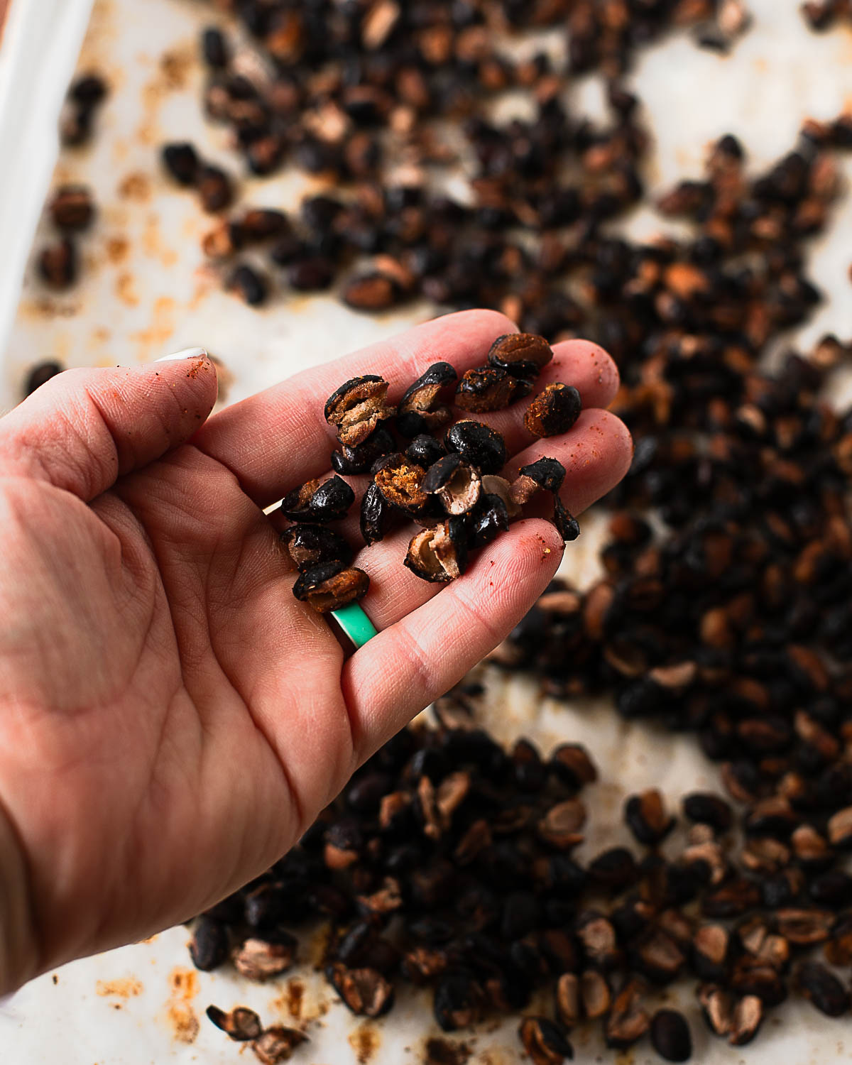 Hand holding a pile of crispy roasted black beans, showing their crunchy split texture.