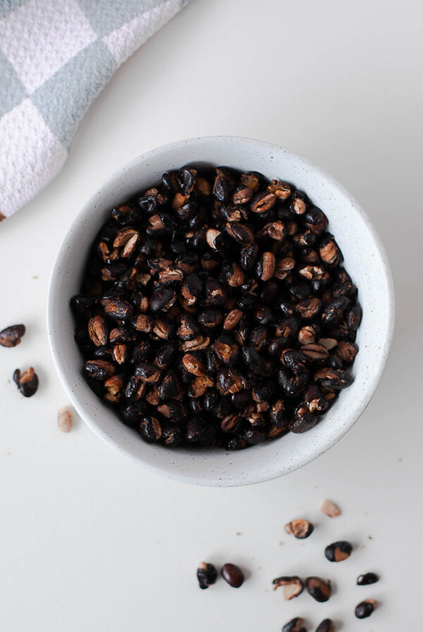 Overhead view of crispy roasted black beans in a small speckled bowl next to a checkered kitchen towel.