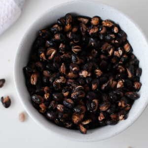 Close-up overhead shot of crispy roasted black beans piled in a small ceramic bowl.