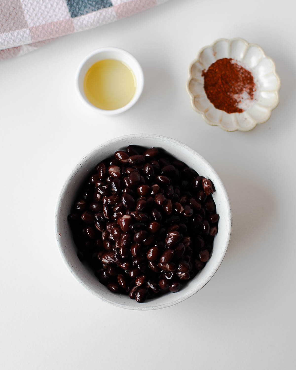 Black beans, avocado oil, and chili seasoning arranged in small bowls, ready to be tossed together for roasting.