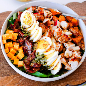 Close-up angled shot of harvest cobb salad with a jar of maple-dijon dressing blurred in the background
