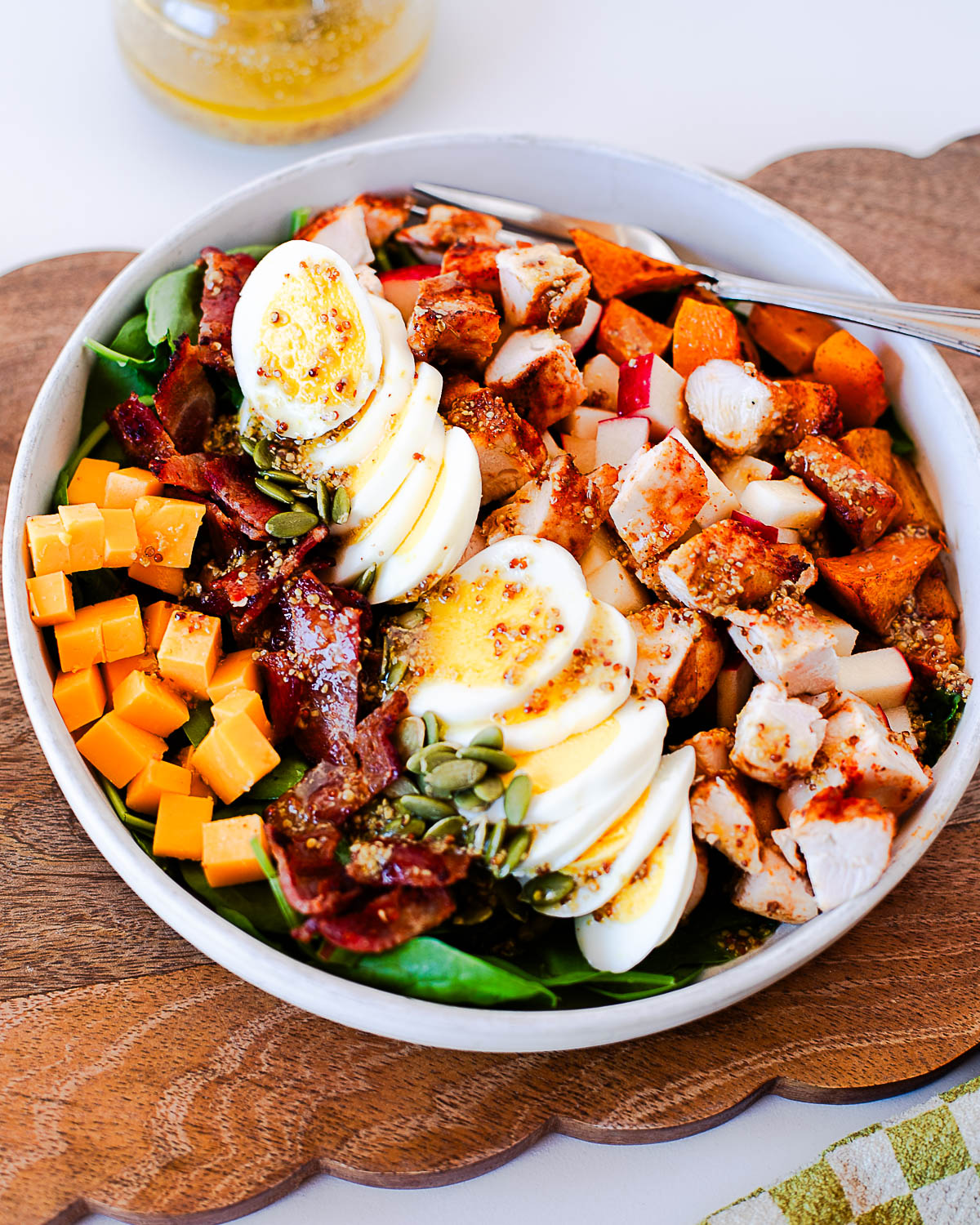 Close-up angled shot of harvest cobb salad with a jar of maple-dijon dressing blurred in the background