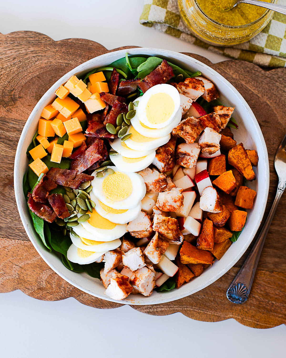 Overhead shot of harvest cobb salad on a wood serving board with a jar of maple-dijon dressing and checkered napkin in the background