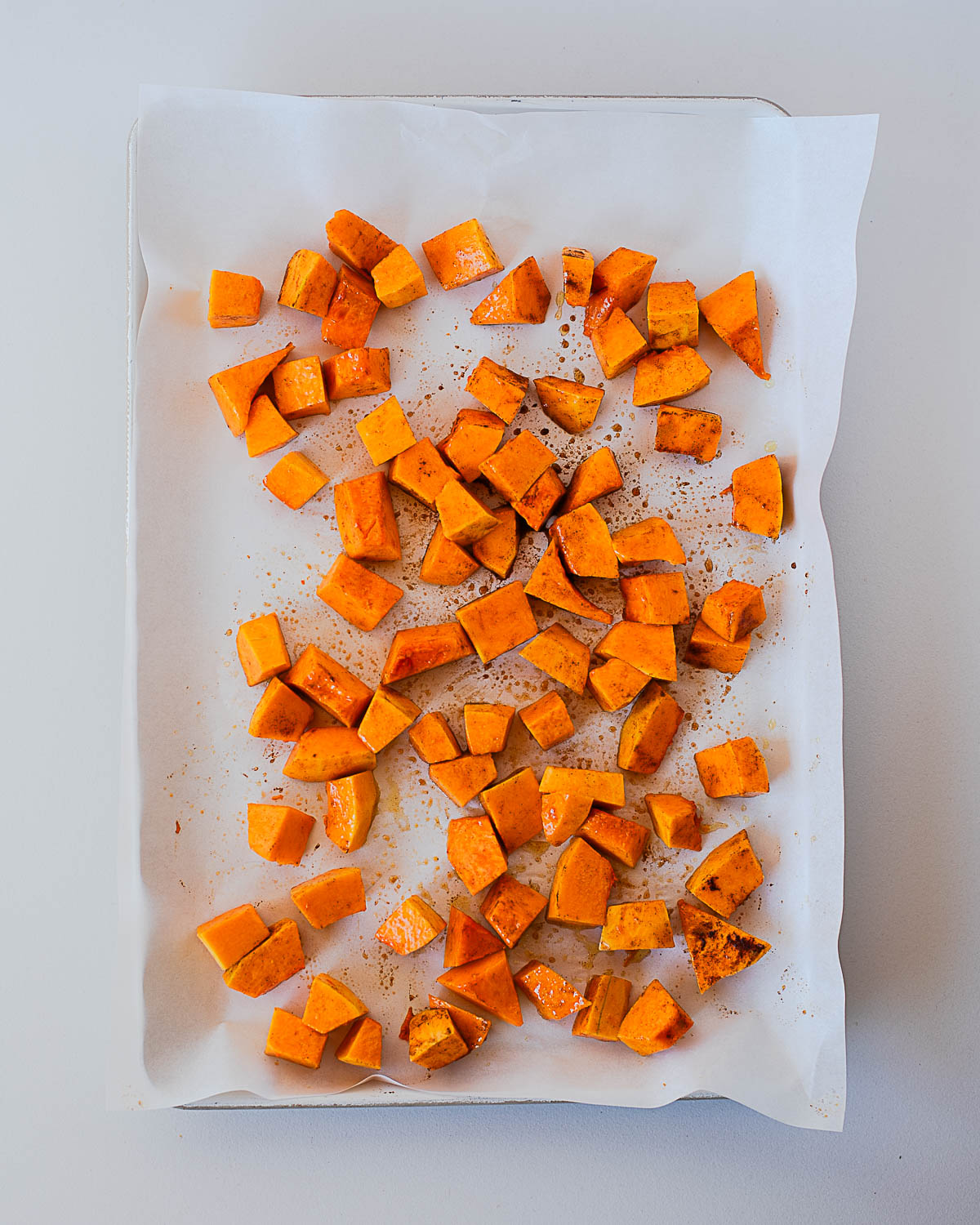 Overhead shot of roasted sweet potato cubes on a parchment-lined baking sheet