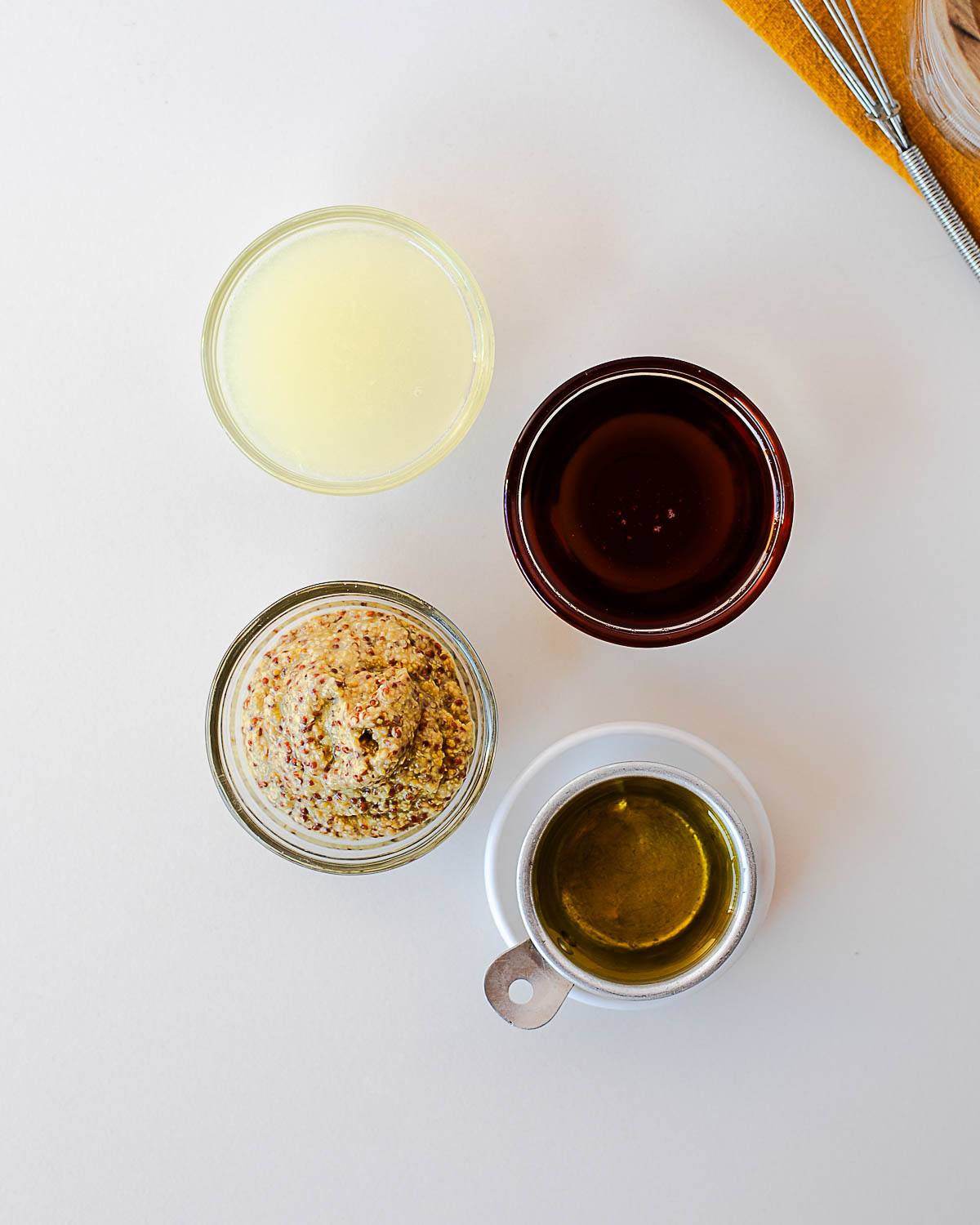 Overhead shot of maple mustard dressing ingredients, lemon juice, maple syrup, Dijon mustard, and olive oil, measured out in small bowls