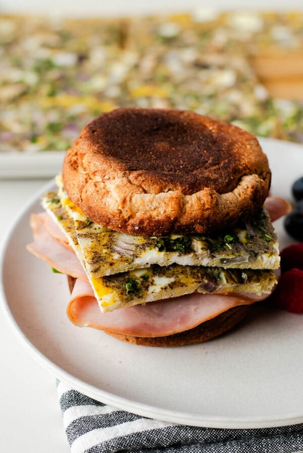 Side view of a breakfast egg sandwich with layered egg bake and ham, berries in the background.