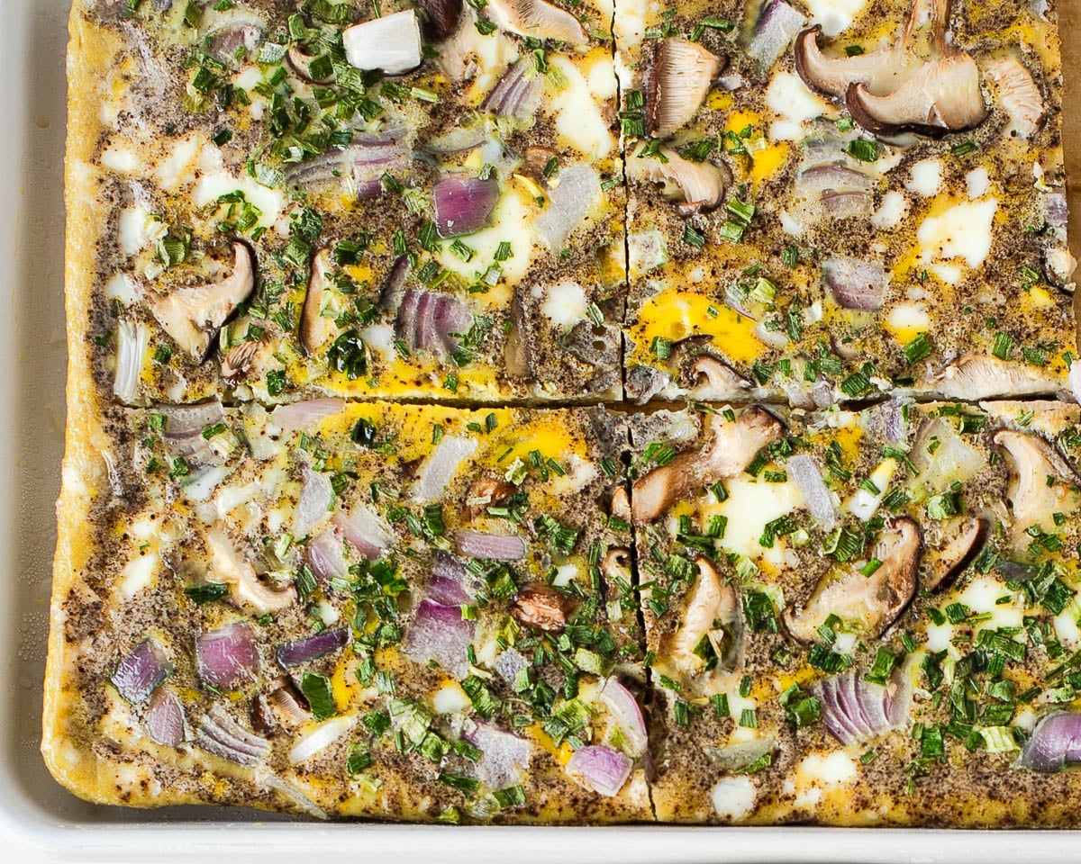 Sheet pan egg bake fully cooked, showing the golden set eggs with mushrooms, red onion, and herbs baked throughout.