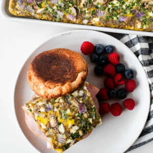 Overhead shot of a plated breakfast sandwich next to fresh berries, with the sheet pan egg bake pan visible in the background.