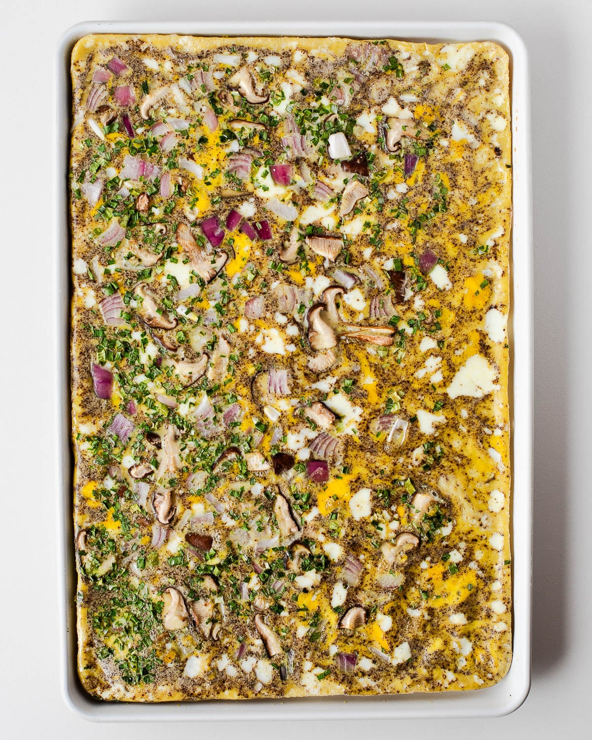 Sheet pan egg bake fully cooked, showing the golden set eggs with mushrooms, red onion, and herbs baked throughout.