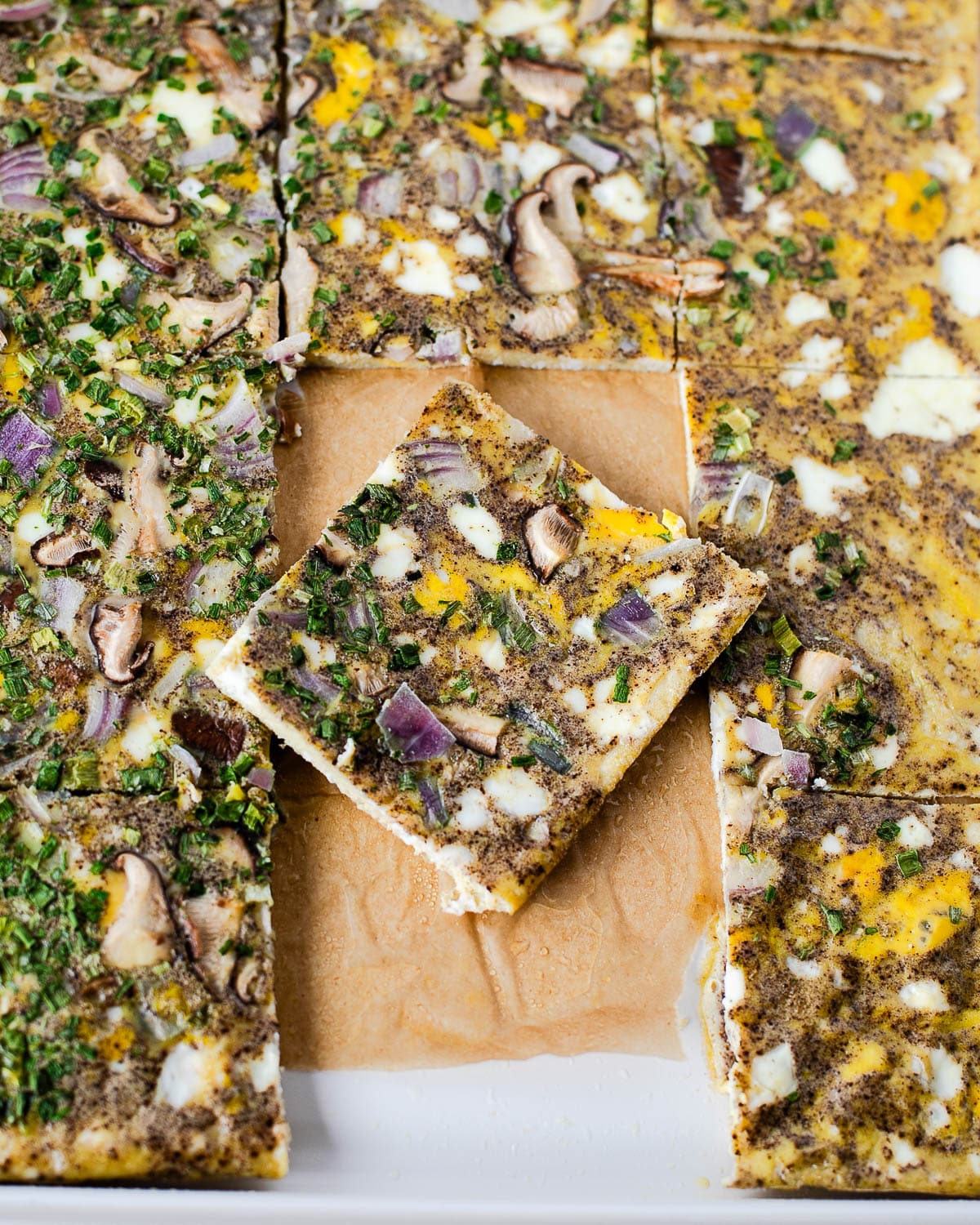 lose-up of a single square of sheet pan egg bake showing the texture of the eggs with mushrooms, onion, and chives.