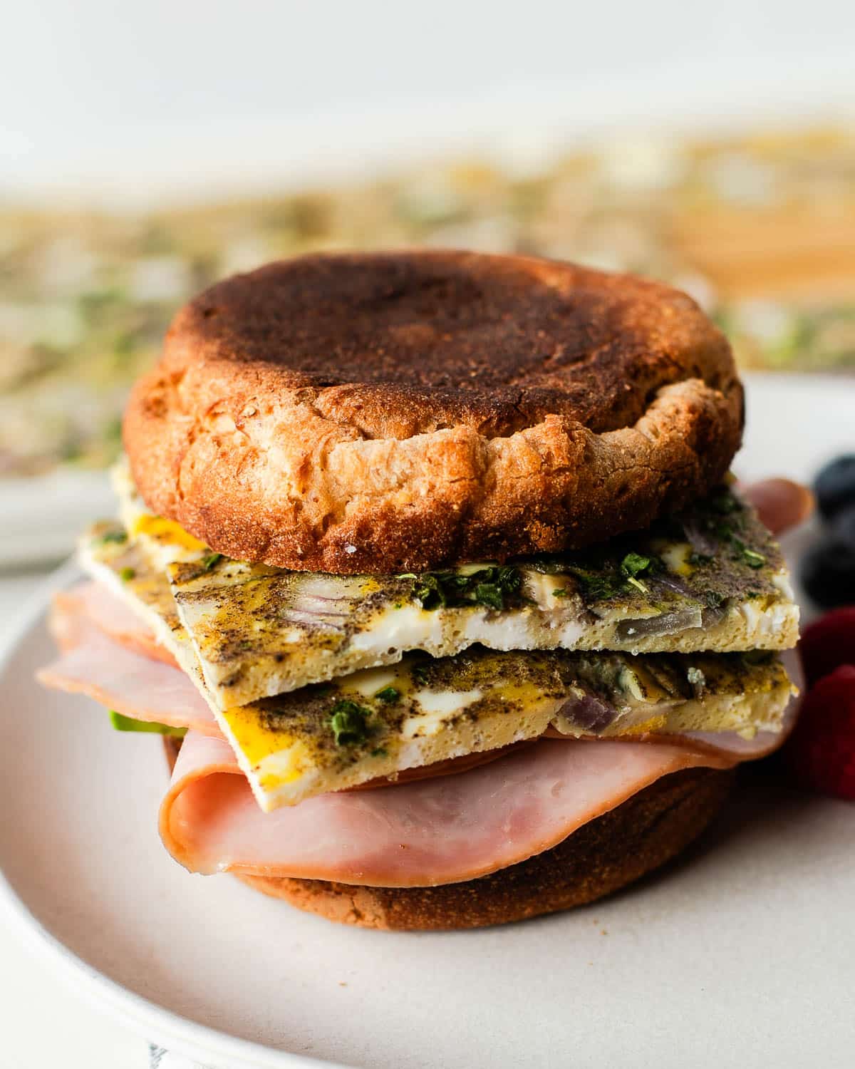 Front view of a finished breakfast sandwich on a plate with raspberries and blueberries.