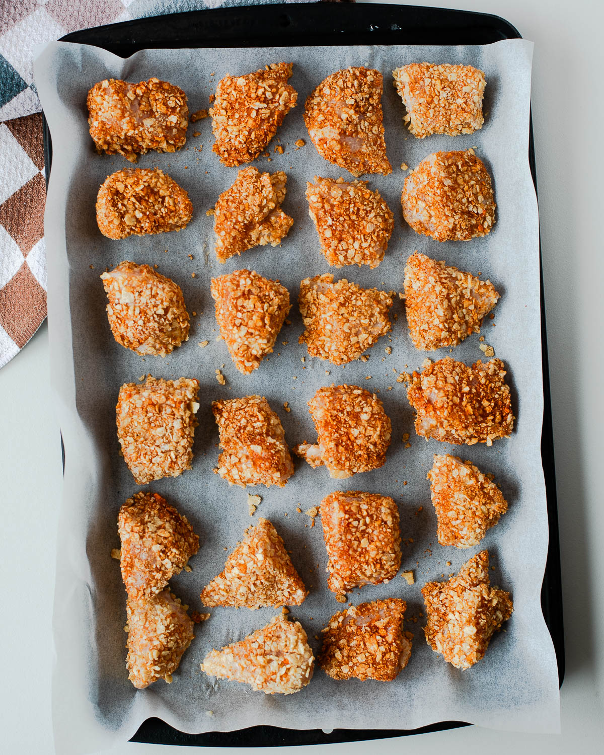 Tortilla chip crusted chicken nuggets coated and arranged on a parchment-lined baking sheet before baking