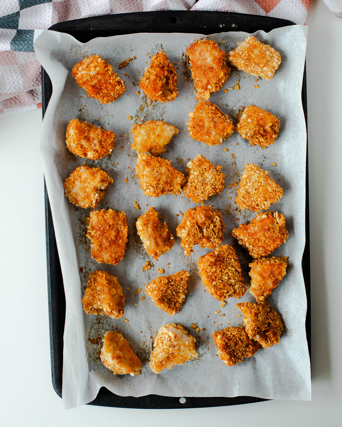 Golden brown tortilla crusted chicken nuggets fresh out of the oven on a baking sheet.