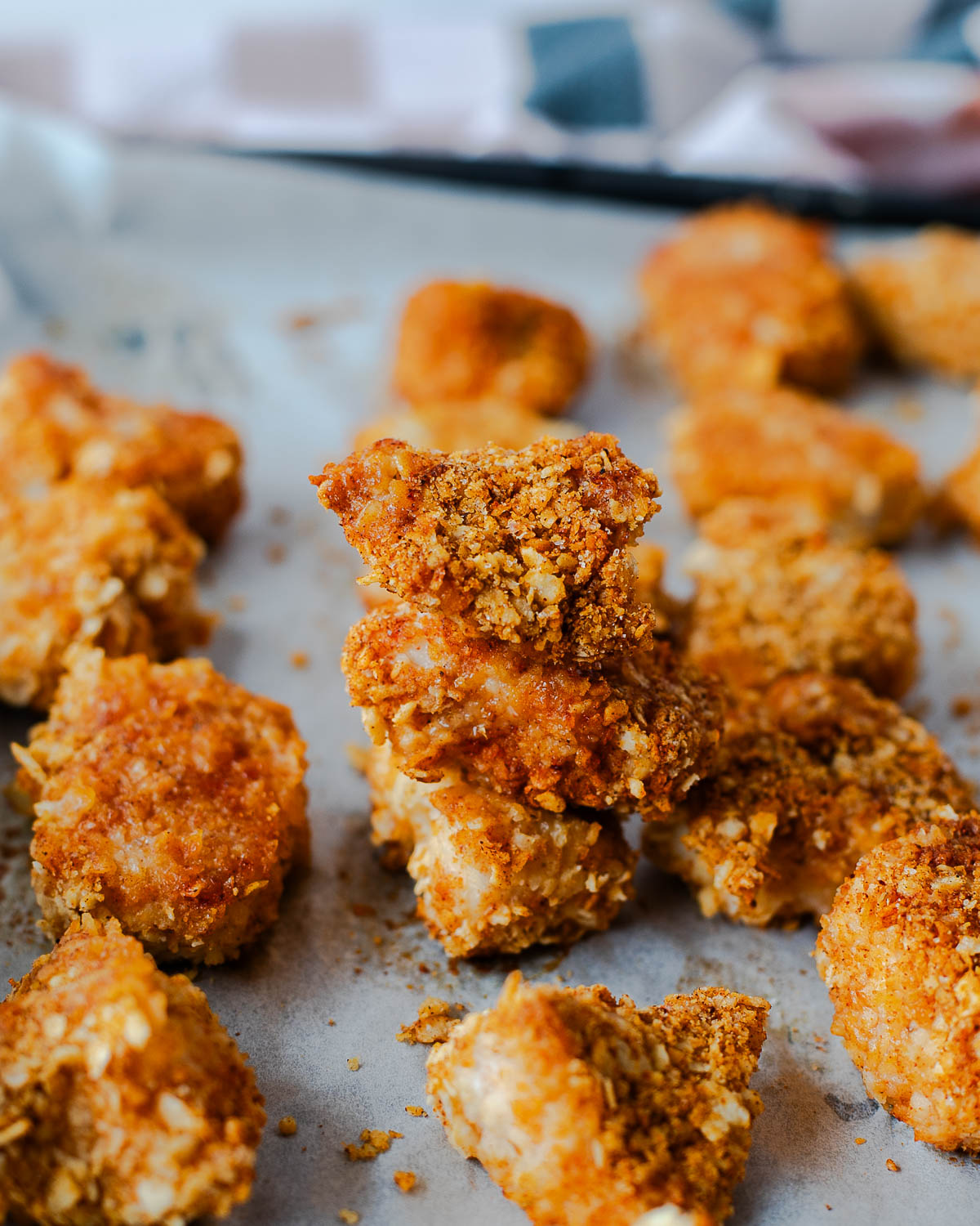 Close-up of crispy tortilla chip crusted chicken nuggets stacked on a baking sheet, showing the crunchy breading.
