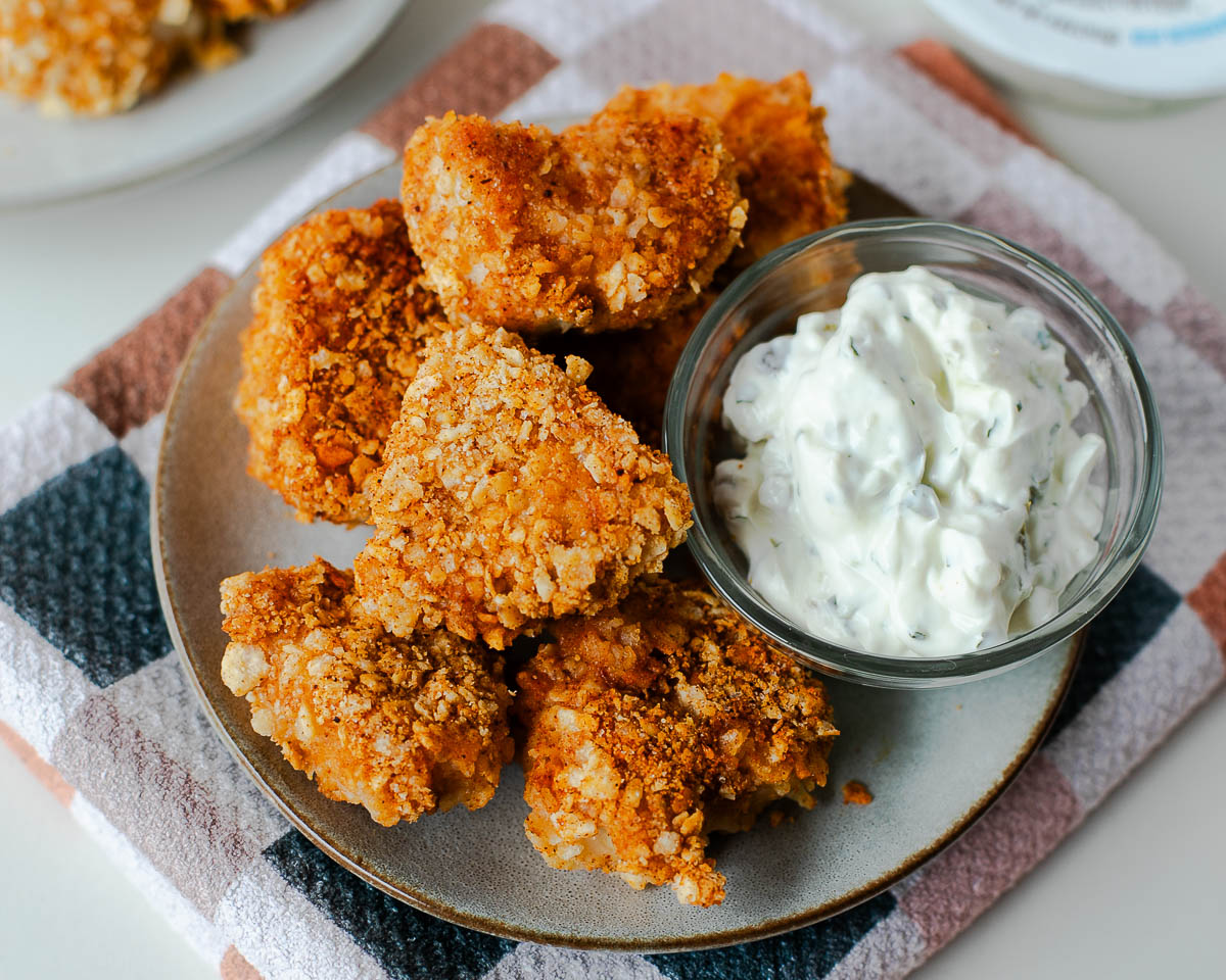 Tortilla crusted chicken nuggets served on a plate with a creamy dipping sauce