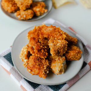 Plates of tortilla chip crusted chicken nuggets with tortilla chips and cherry tomatoes on the side.