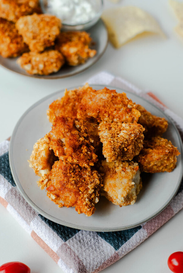 Plates of tortilla chip crusted chicken nuggets with tortilla chips and cherry tomatoes on the side.