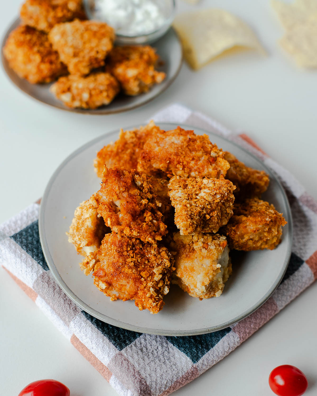 Plates of tortilla chip crusted chicken nuggets with tortilla chips and cherry tomatoes on the side.