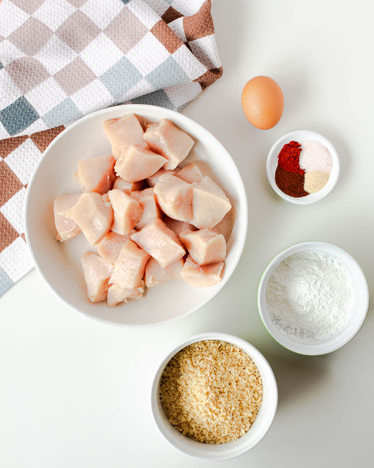 Cubed chicken breast, egg, corn starch, tortilla chip crumbs, and spices laid out for tortilla crusted chicken nuggets.