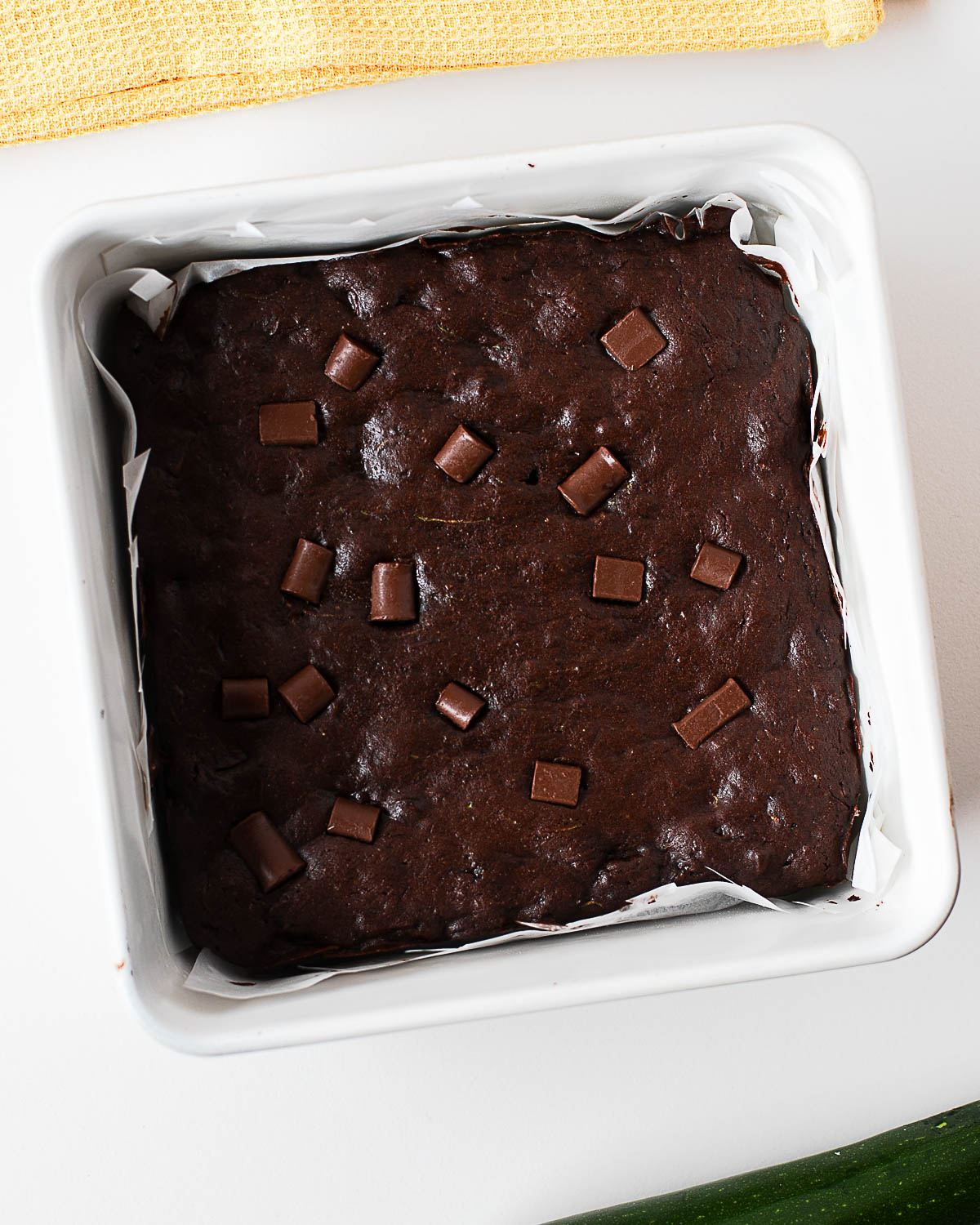 Baked zucchini brownies in a parchment-lined pan, golden chocolate chunks melted across the top.