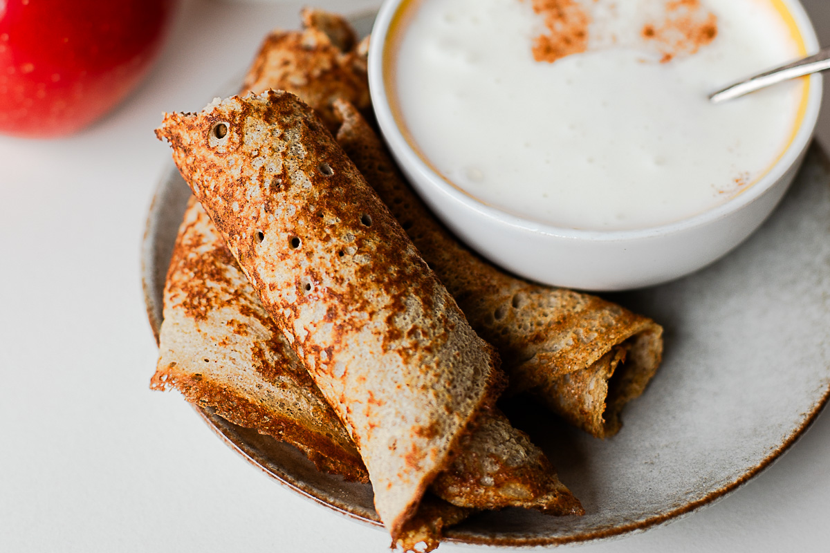 Apple crepes on a plate with a bowl of creamy honey dip