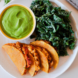 Overhead view of crispy baked chicken tacos on a plate with green avocado dip and kale salad