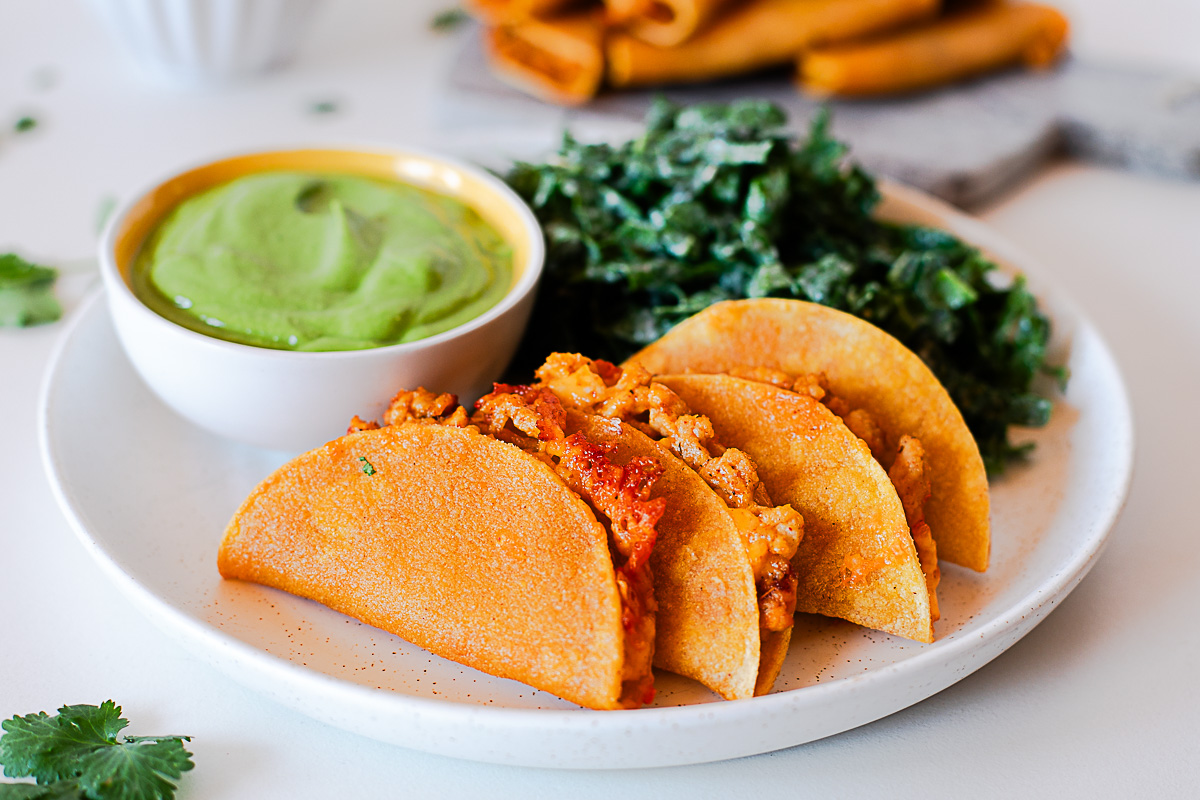 Baked chicken tacos on a plate with green avocado dip and kale salad