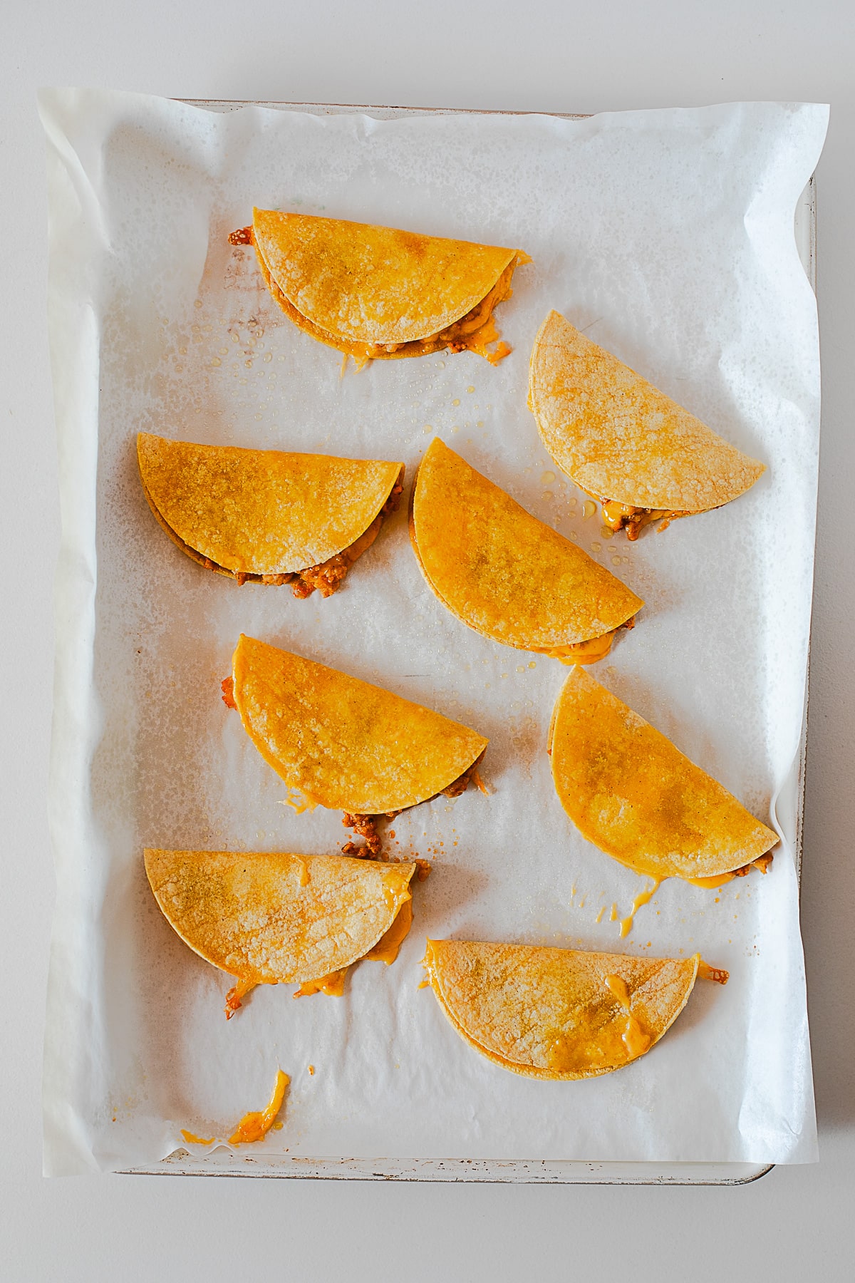 Folded corn tortillas filled with chicken and melted cheese on a baking sheet