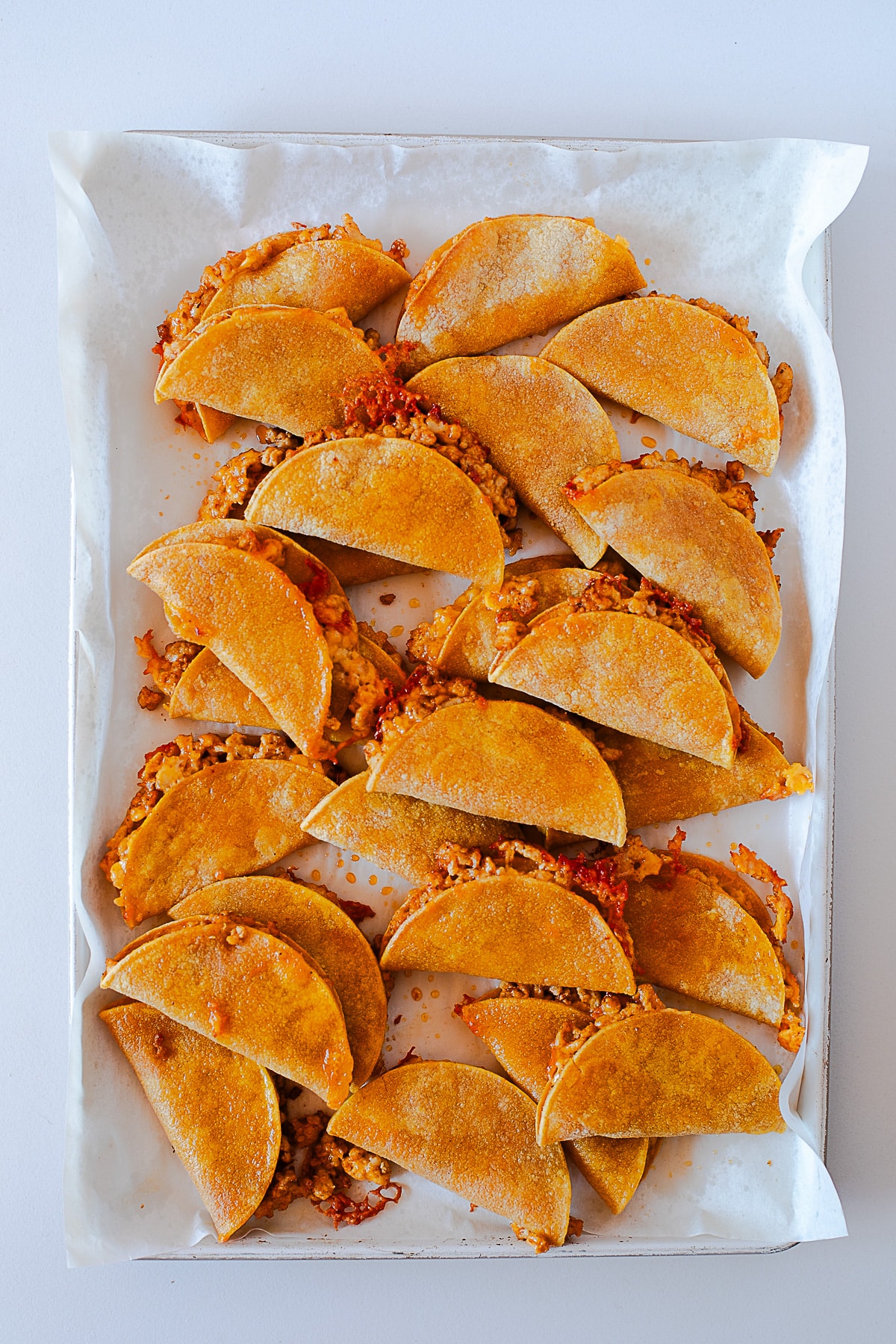 Golden, crispy baked chicken tacos on a parchment lined sheet pan