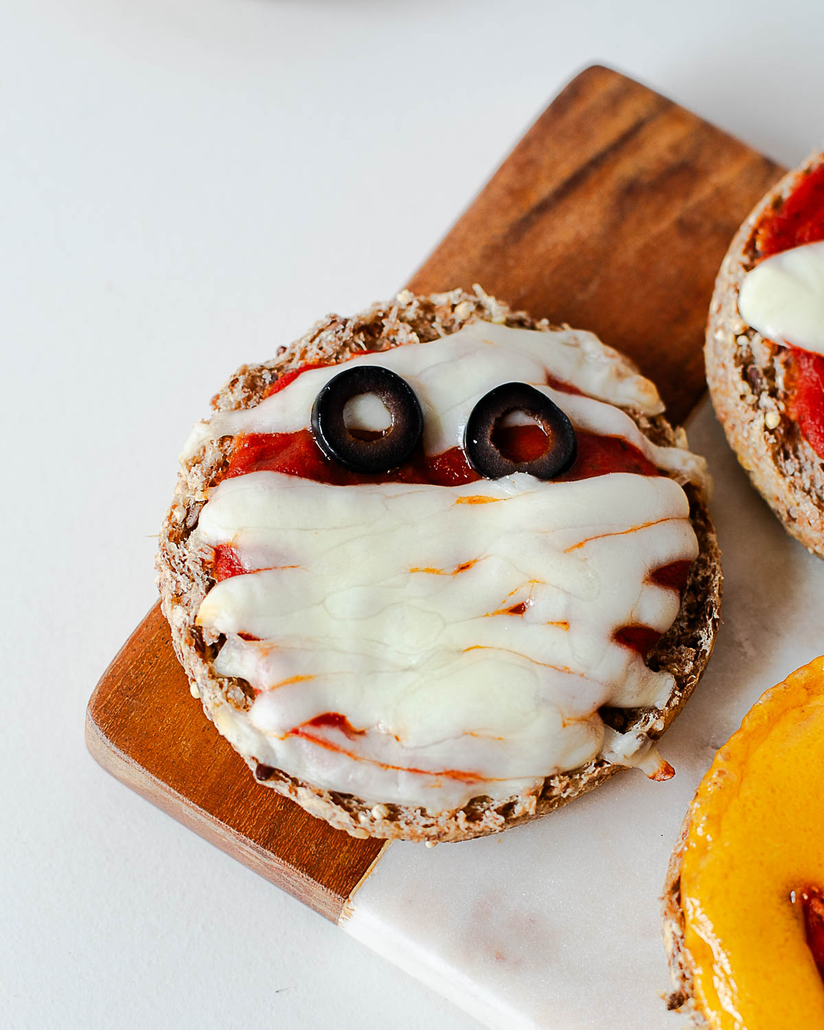 Close-up of a mummy Halloween mini pizza with string cheese strips and black olive eyes.