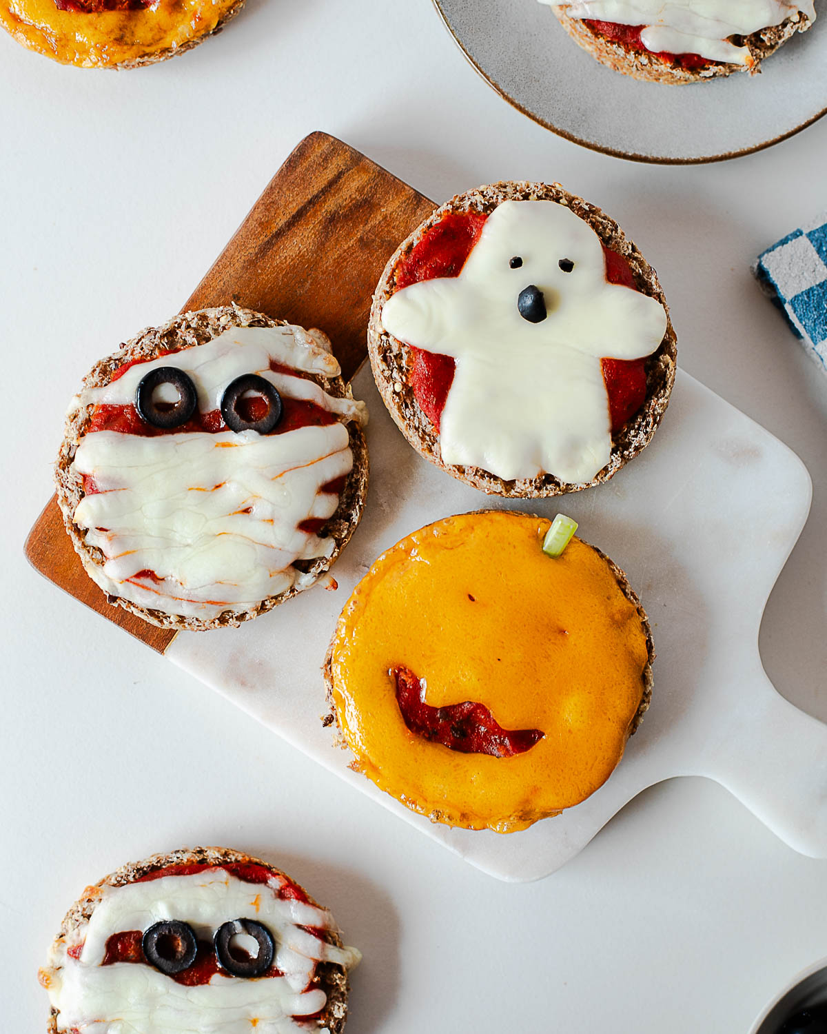 Three Halloween mini pizzas arranged on a cutting board, showing mummy, ghost, and jack-o'-lantern designs.