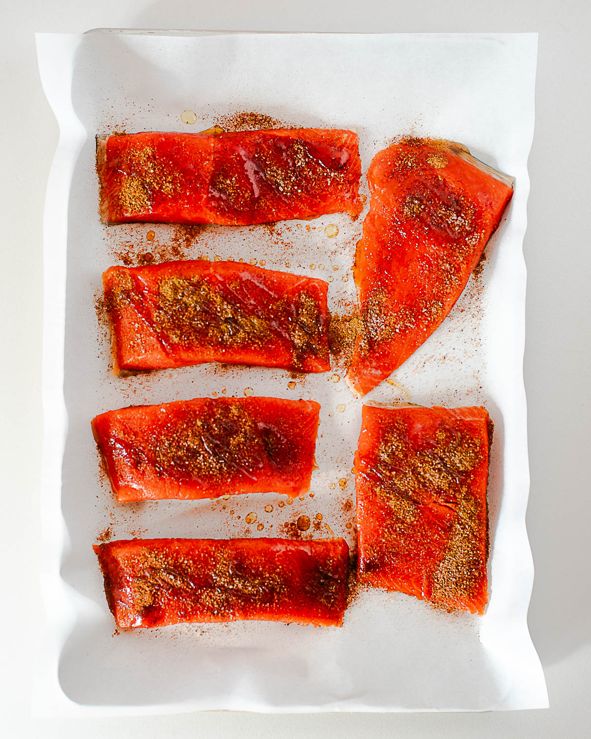 Raw seasoned salmon fillets on a parchment lined baking sheet, drizzled with hot honey before baking